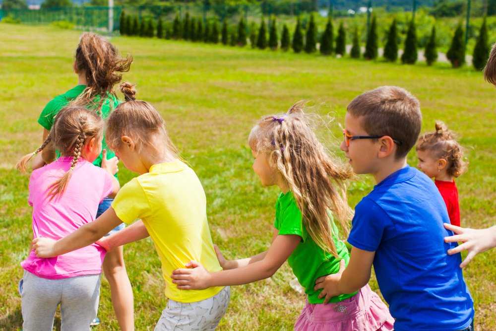 Ребенок играет со сверстниками. Дети в лагере обнимаются. Ребенок со сверстниками. Общение детей. Общение детей со сверстниками.